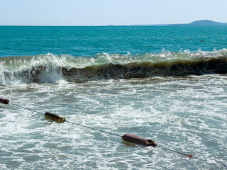 Waves crash on a shoreline with floating buoys during daytime at a beach © DSMT