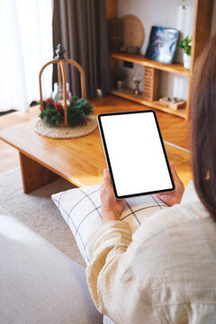 Vertical mockup image of a woman holding tablet with blank desktop white screen at home