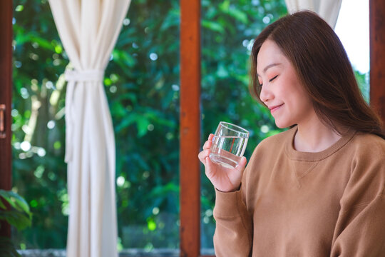 Portrait image of a woman holding and drinking water at home