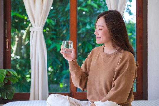 Portrait image of a woman holding and drinking water on the bed at home