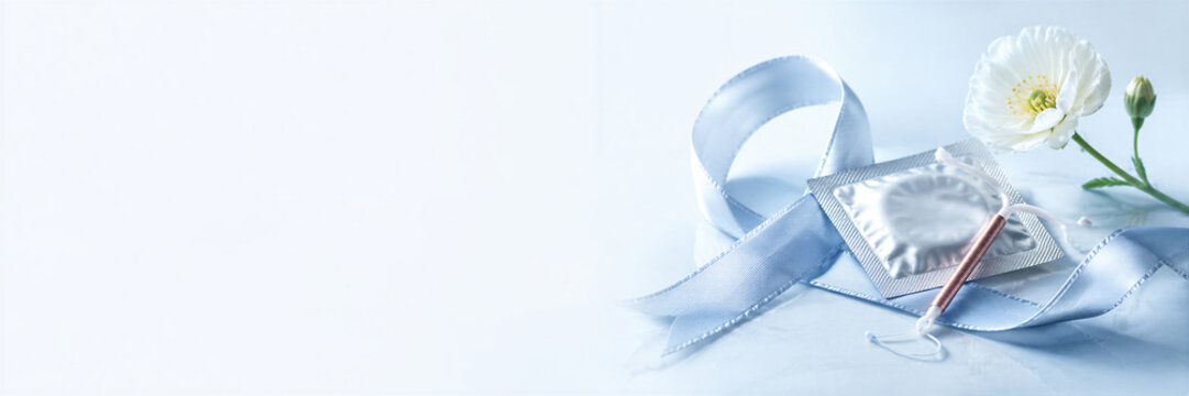 Contraceptive devices rest on a ribbon beside a flower. A condom packet and copper IUD support informed family planning. World Contraception Day raises Banner with copy space