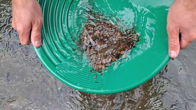 Slow motion of a process of washing rock in a stream using a prospector's pan; close-up camera shot of beautiful river pebbles.