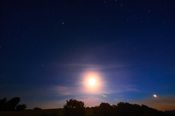 Moon on a twilight sky with stars, planets and landscape mountain silhouettes. © astrosystem
