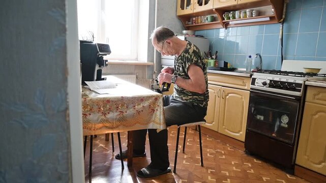 Senior man working and fixing small device on a kitchen table at home