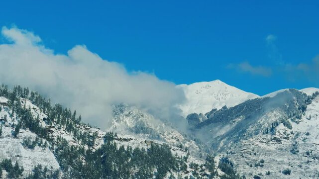 4K Landscape shot of clouds covering the snowy Himalayan mountain peak after fresh snowfall during the winter season as seen from Manali in Himachal Pradesh, India. Scenic natural landscape background