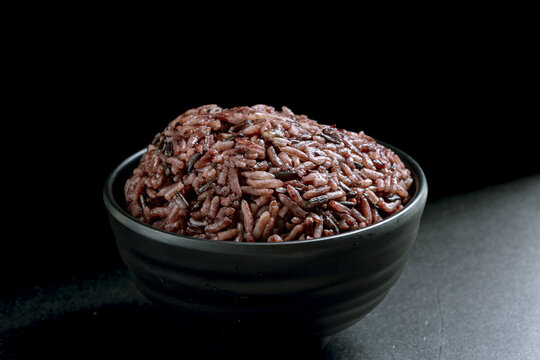 Steamed black rice, healthy whole grain, served in black ceramic bowl on dark background, nutritious food, simple and rustic style, close up