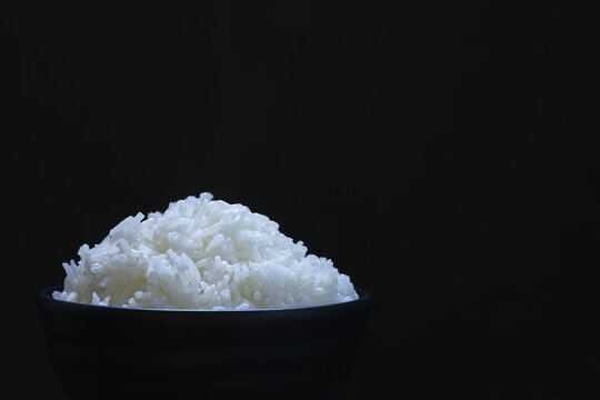 Steamed white rice cooked fluffy texture in black bowl isolated on dark background simple food Asian cuisine minimal style comfort meal soft lighting appetizing