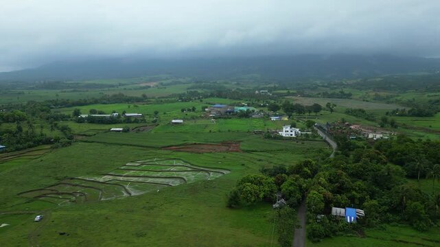 Moody aerial footage of rice-growing countryside near Villaflorida, Ocampo, Camarines Sur, with lush farms and agricultural fields stretching toward Mount Isarog beneath heavy tropical cloud cover.