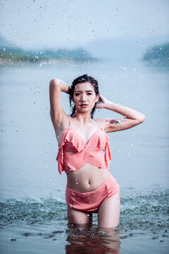 Joyful Asian woman cooling off in natural water splash during summer vacation, enjoying refreshed freedom.