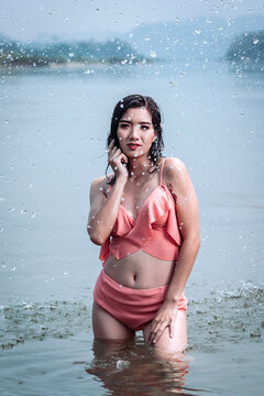 Joyful Asian woman cooling off in natural water splash during summer vacation, enjoying refreshed freedom.