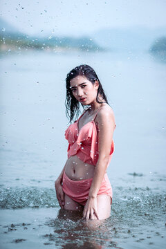 Joyful Asian woman cooling off in natural water splash during summer vacation, enjoying refreshed freedom.