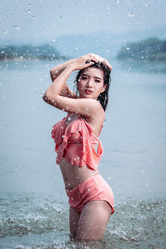 Joyful Asian woman cooling off in natural water splash during summer vacation, enjoying refreshed freedom.