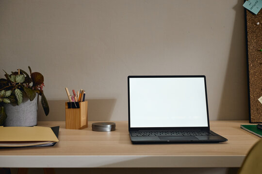 Laptop with blank screen standing on wooden desk in home office workspace. Ideal mockup template for remote work technology, e-learning website, corporate software presentation
