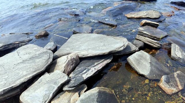 Footage of a large, flat flagstone-like rock on a rocky beach area of Manitoulin Island, Ontario, Canada. The exposed bedrock and shoreline setting highlight the rugged geological character of the isl