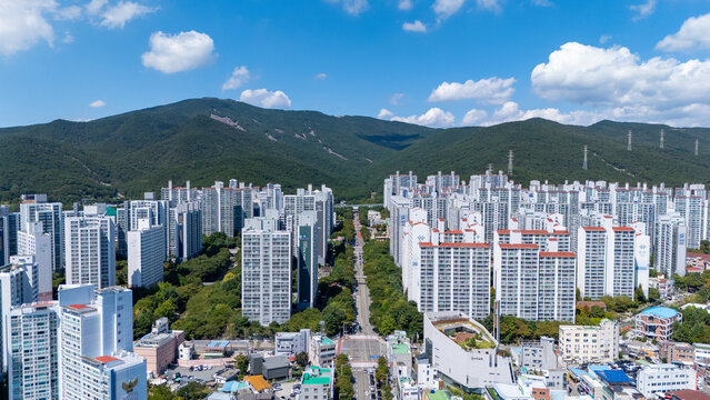 Aerial view of Yangun-ro surrounded by dense high-rise apartment complexes and lush green mountains under a bright blue sky in Busan, Busan, South Korea.