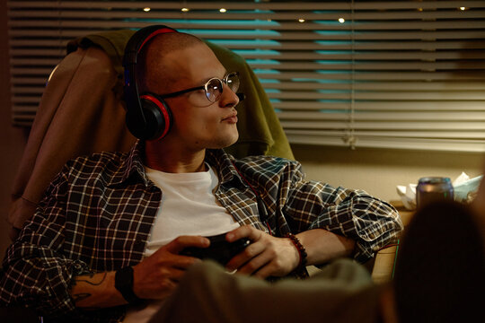 Young adult Caucasian man wearing headphones holding gamepad while playing video games with friend. Useful for gaming advertising, entertainment campaigns, digital lifestyle content
