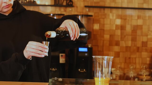 Barwoman measures caramel syrup with jigger at countertop closeup. Female barkeeper prepares delicious cocktail ingredients in coffeeshop