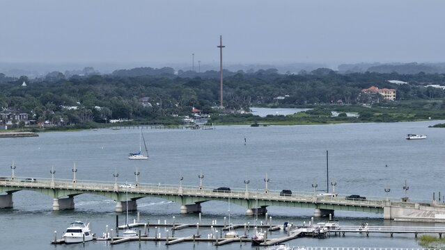 Aerial view of the Bridge of Lions spanning the Matanzas River with the Great Cross in the distance, boats at the marina, and coastal vegetation in St. Augustine, Florida, United States.