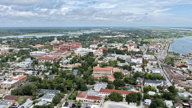 Aerial view of the historic city of St. Augustine featuring Spanish colonial architecture, lush green trees, and the waterfront under a cloudy sky in St. Augustine, Florida, United States.