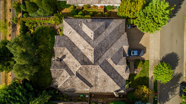 Aerial view of a residential house with a complex shingled roof surrounded by lush green trees and a driveway in Lake Oswego, Oregon, United States.