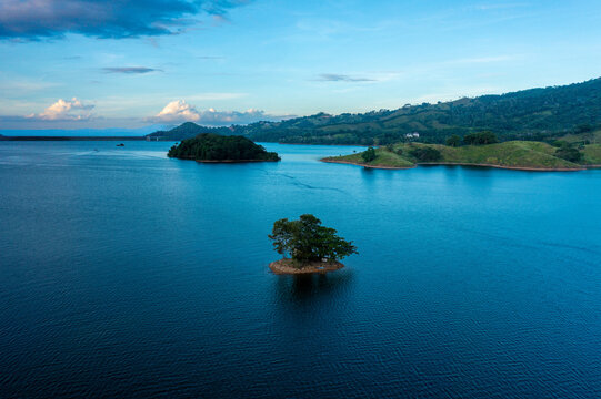 Aerial view of the Hatillo dam wall and a small island with trees in the middle of the reservoir surrounded by lush green hills in Cotui, Sanchez Ramirez, Dominican Republic.