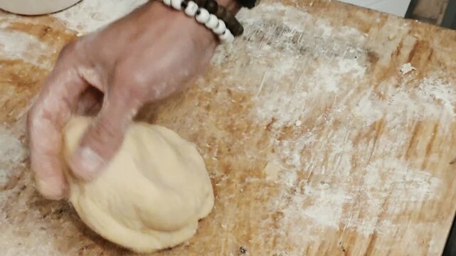 Man kneading dough with hands on floured wooden table. Homemade pastry preparation with eggshells in bowl