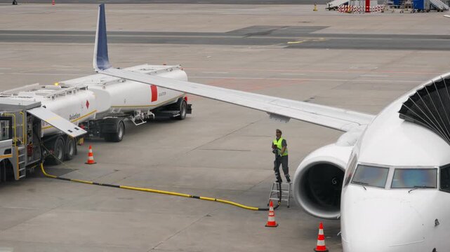 Commercial airplane refueling process on airport runway apron with fuel truck hose connected to jet aircraft wing tank for aviation logistics maintenance industry infrastructure service safety.