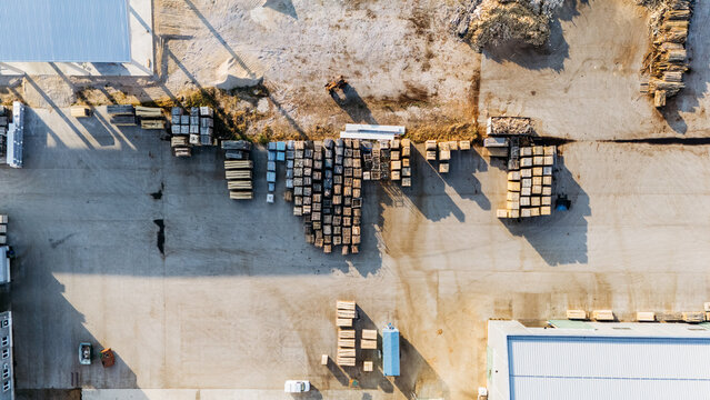 Aerial view of a lumber yard with organized stacks of timber and wooden pallets on a paved industrial site in Sremska Mitrovica, Vojvodina, Serbia.