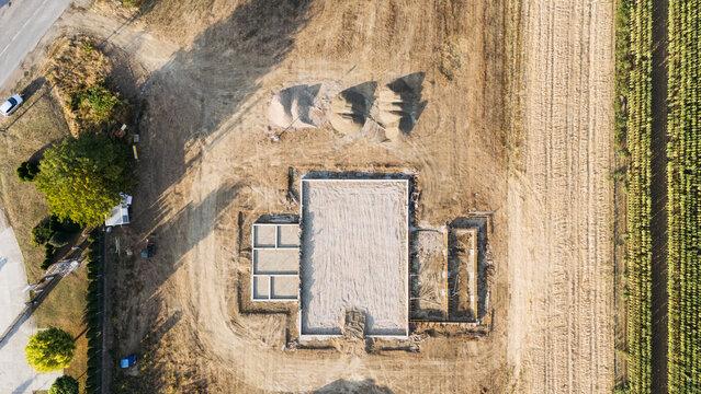 Aerial view of a construction site showing building foundations, piles of sand, and surrounding agricultural land in Sremska Mitrovica, Vojvodina, Serbia.