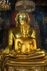 Obraz premium A vertical interior shot of the sacred twin golden Phra Phuttha Chinnasi and Phra Suwannakhet Buddha statues inside Wat Bowonniwet Vihara temple.