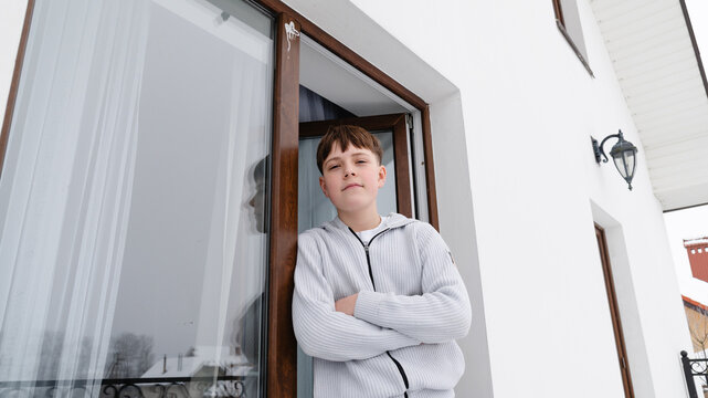 Boy stands at an open window in a snowy setting during winter time