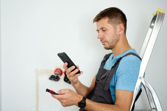 Man using smartphone during wall outlet installation