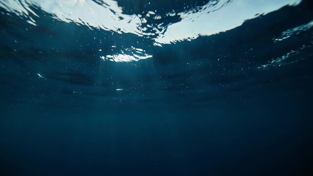 Sunlight shafts pierce deep blue ocean surface waves from below with gentle motion