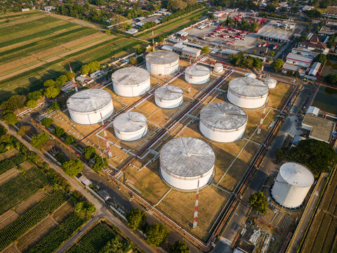 Aerial view of a fuel storage depot with large white cylindrical tanks and complex pipeline infrastructure surrounded by agricultural fields in Boyolali, Central Java, Indonesia.