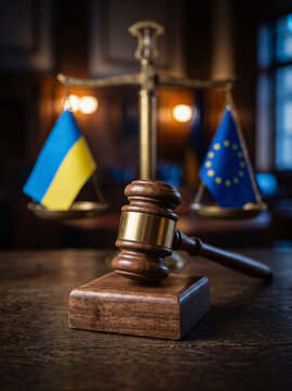 wooden judge gavel on stand before scale bowls with small flags of ukraine and european union in dark court room