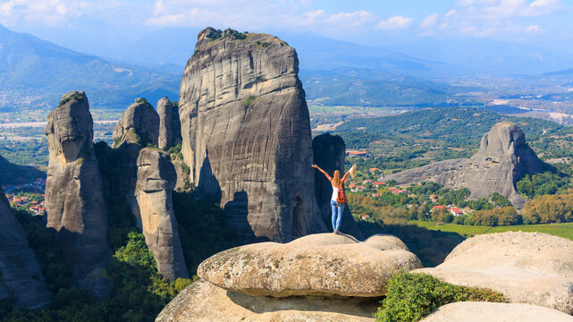 Woman Tourist Standing on Rock Cliff with Arms Raised Overlooking Meteora Valley in Greece