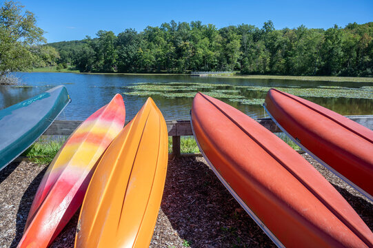 Colorful kayaks on the shore of idyllic Pennsylvania lake calm water, woodland state park background with copy space travel vacation outdoor adventure