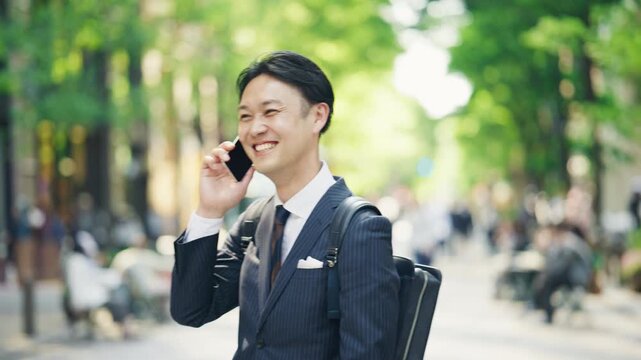 Japanese businessman walking and talking on the phone with a briefcase