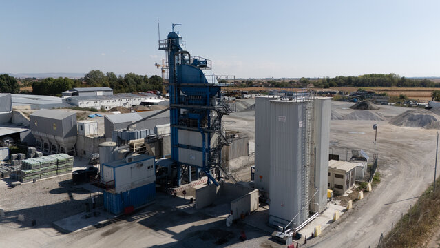 Aerial view of the TASYAPI industrial facility featuring a blue asphalt plant tower and white storage silos surrounded by gravel piles in Kuzmin, Vojvodina, Serbia.