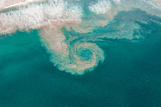 Aerial view of Huntington Beach showing a swirling sediment plume in the turquoise ocean water near the sandy coastline in Huntington Beach, California, United States.