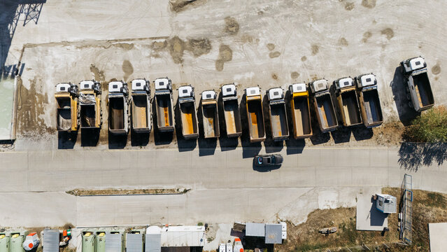 Aerial view of a row of dump trucks parked in a line on a gravel lot in Kuzmin, Vojvodina, Serbia.