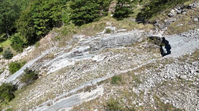 Ripresa aerea zenitale di un arido pendio montano caratterizzato da stratificazioni rocciose, pietraie calcaree e radi cespugli di vegetazione