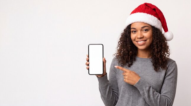 Woman wearing Santa hat points at smartphone screen with blank display, festive attire, and neutral background suitable for holiday promotions