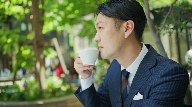 Businessman drinking coffee at a tree lined outdoor cafe