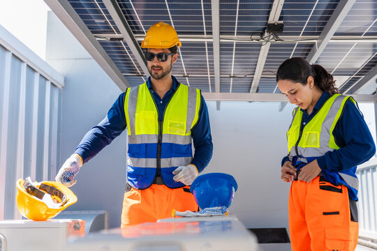 Engineers checking photovoltaic system infrastructure at solar power plant, male and female solar energy technicians working together on renewable power installation project