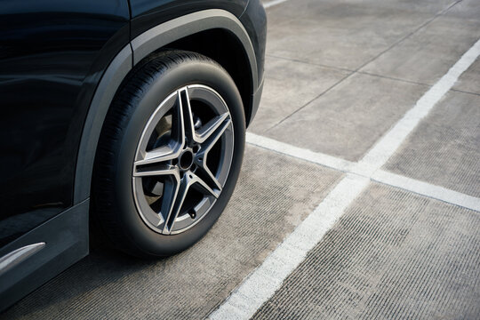 black SUV side profile focusing on the rear wheel parked inside a concrete parking space outlined by clean white lines, car parked in the right position in outdoor shopping plaza carpark area