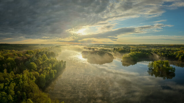 Aerial view of Venekotensee at sunrise with mist rising over the water and surrounding forest in Niederkruchten, Nordrhein-Westfalen, Germany.