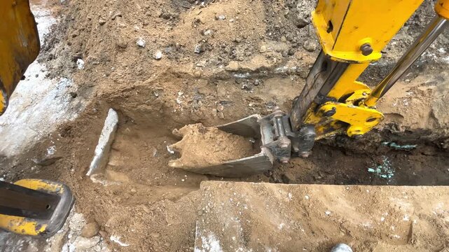 Yellow excavator bucket digging narrow trench on construction site, ground earthworks, heavy equipment, utility installation, Industry