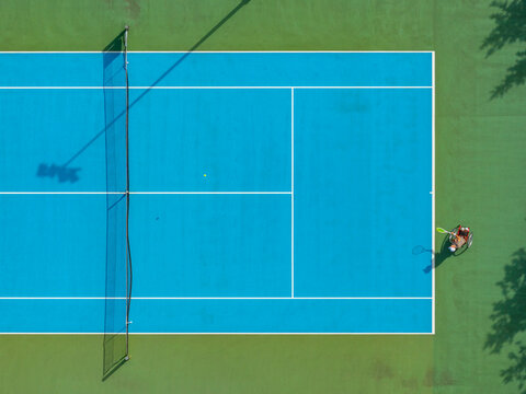 Aerial view of a wheelchair tennis match on a vibrant blue court with a player in a wheelchair holding a racket in Poland.