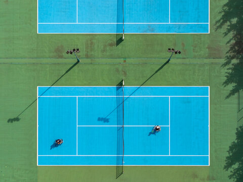 Aerial view of a wheelchair tennis match on a blue court with players in wheelchairs, net, and court markings in Poland.